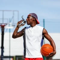 jugador-africano-de-baloncesto-bebiendo-agua-una-botella-en-cancha-al-aire-libre-joven-afroamericano-bebe-187242753